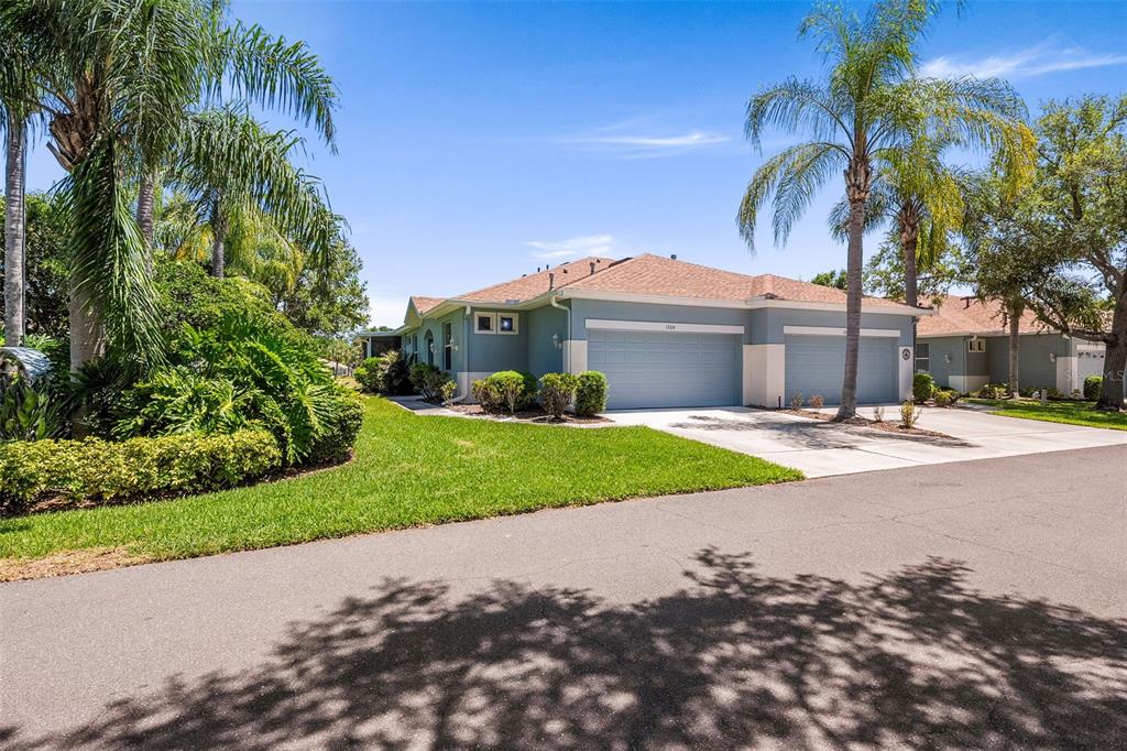 A light blue single-story house with a two-car garage and palm trees in the yard — 1204 HUNTINGTON GREENS DRIVE UNIT 1204, SUN CITY CENTER, FL