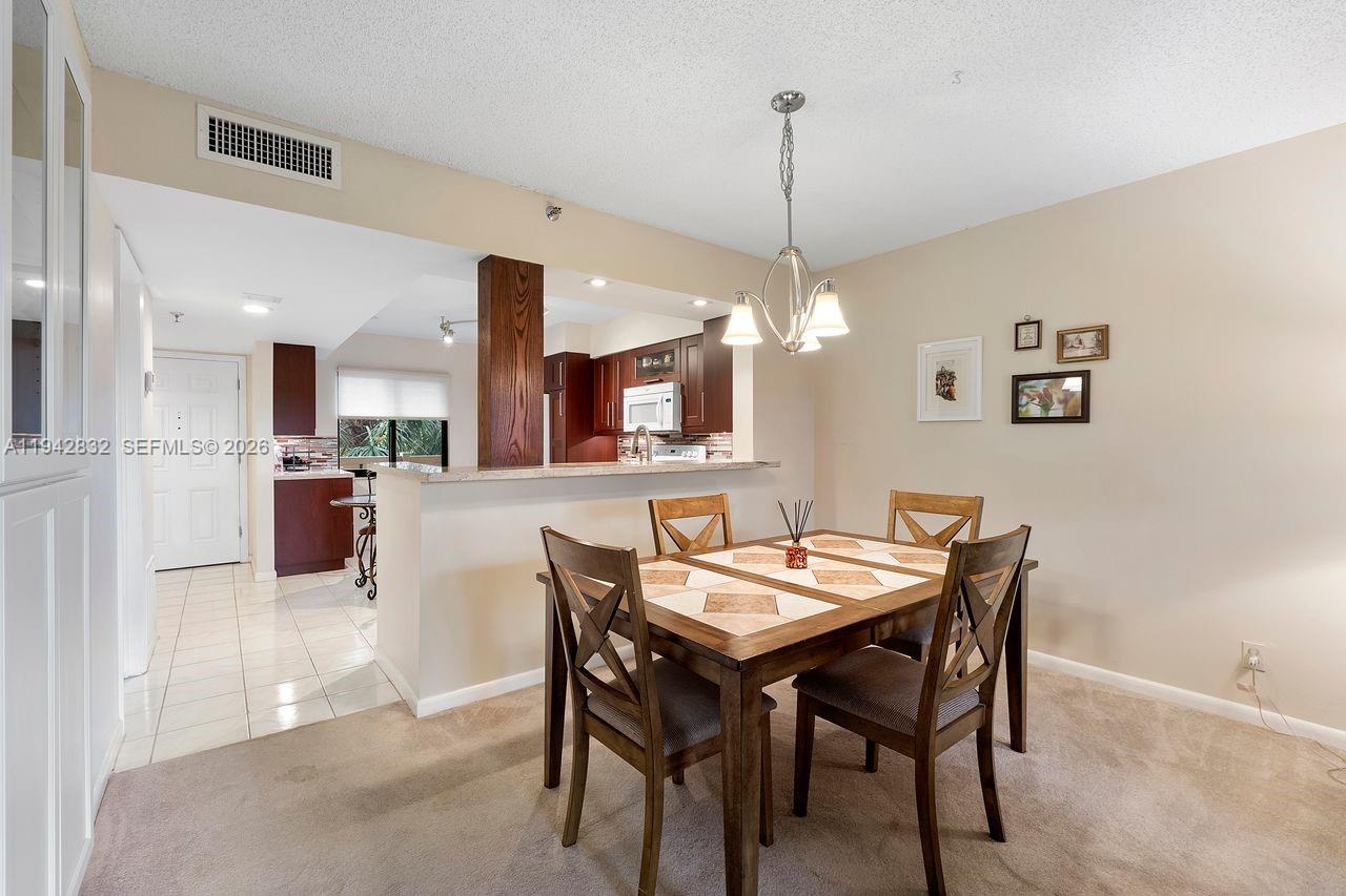 A dining area with a wooden table and chairs sits adjacent to an open kitchen — 2200 S Cypress Bend Dr # 406, Pompano Beach FL 33069, POMPANO BEACH, FL