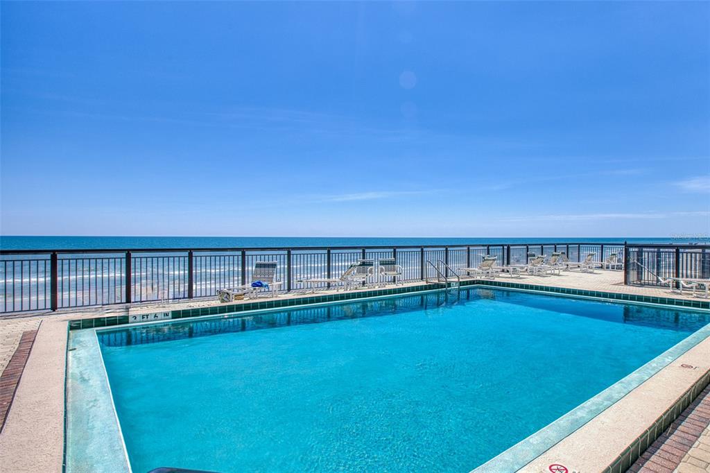 A rectangular swimming pool overlooks the ocean from a paved deck with lounge chairs — 3405 S ATLANTIC AVENUE UNIT 202, NEW SMYRNA BEACH, FL