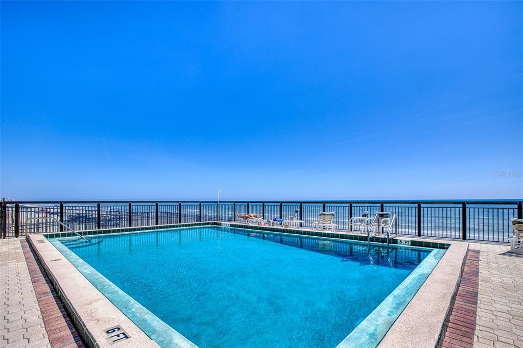 An outdoor swimming pool overlooks the ocean from a paved deck with a metal railing — 3405 S ATLANTIC AVENUE UNIT 202, NEW SMYRNA BEACH, FL