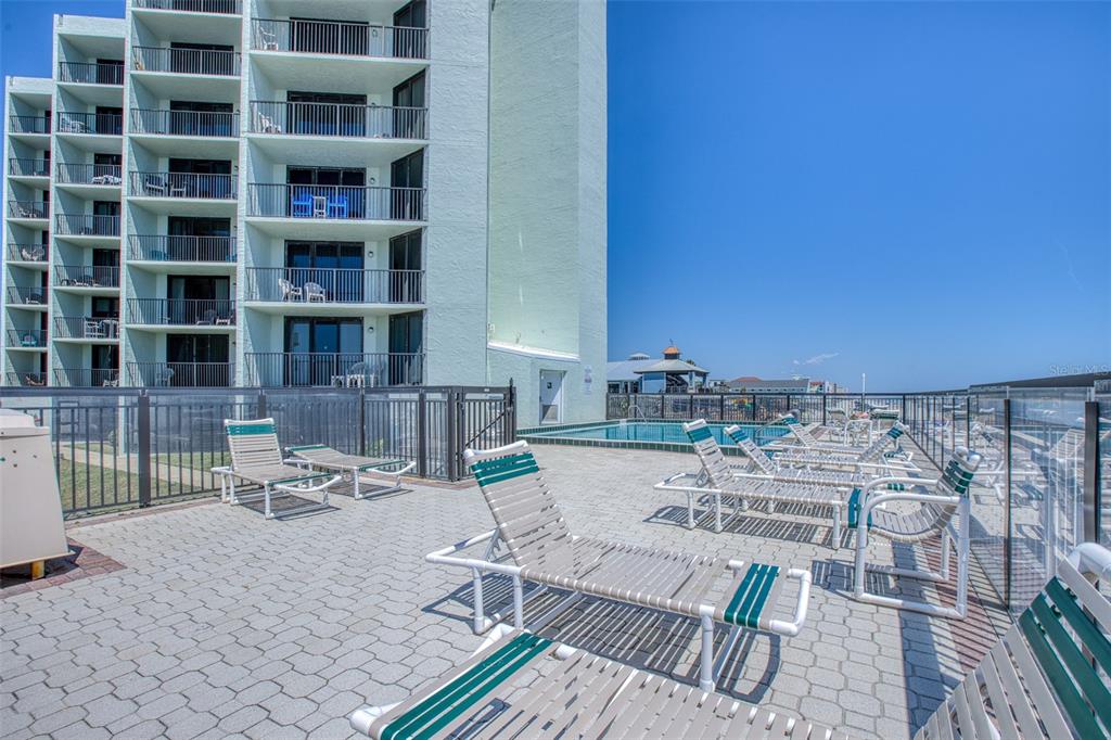 A paved pool deck features lounge chairs next to a multi-story building under a clear sky — 3405 S ATLANTIC AVENUE UNIT 202, NEW SMYRNA BEACH, FL