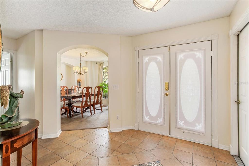An entryway with tile flooring, double glass-paneled doors, and an arched opening to a dining room — 3920 RUNNING WATER DRIVE, ORLANDO, FL