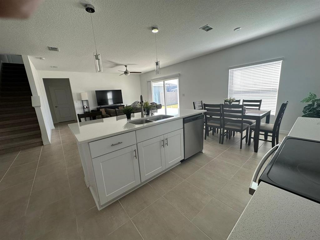 A kitchen with a white island and stainless steel appliances overlooks an open dining area — 5656 COSTA BLANCA WAY, DAVENPORT, FL