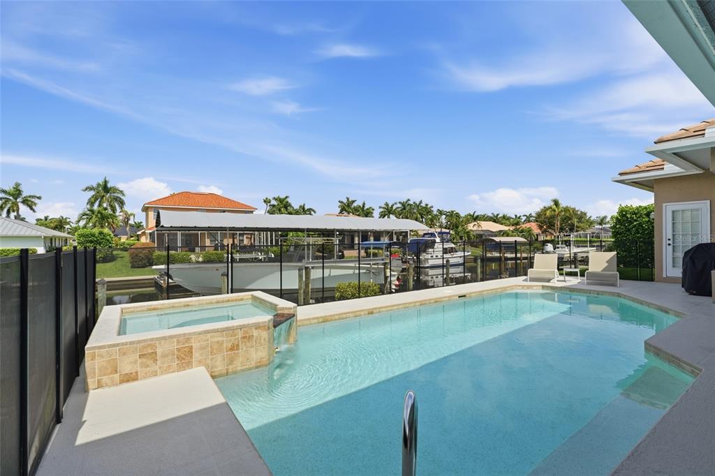 A swimming pool and spa with a water feature overlook a canal with docked boats — 5020 SW 8TH PLACE, CAPE CORAL, FL