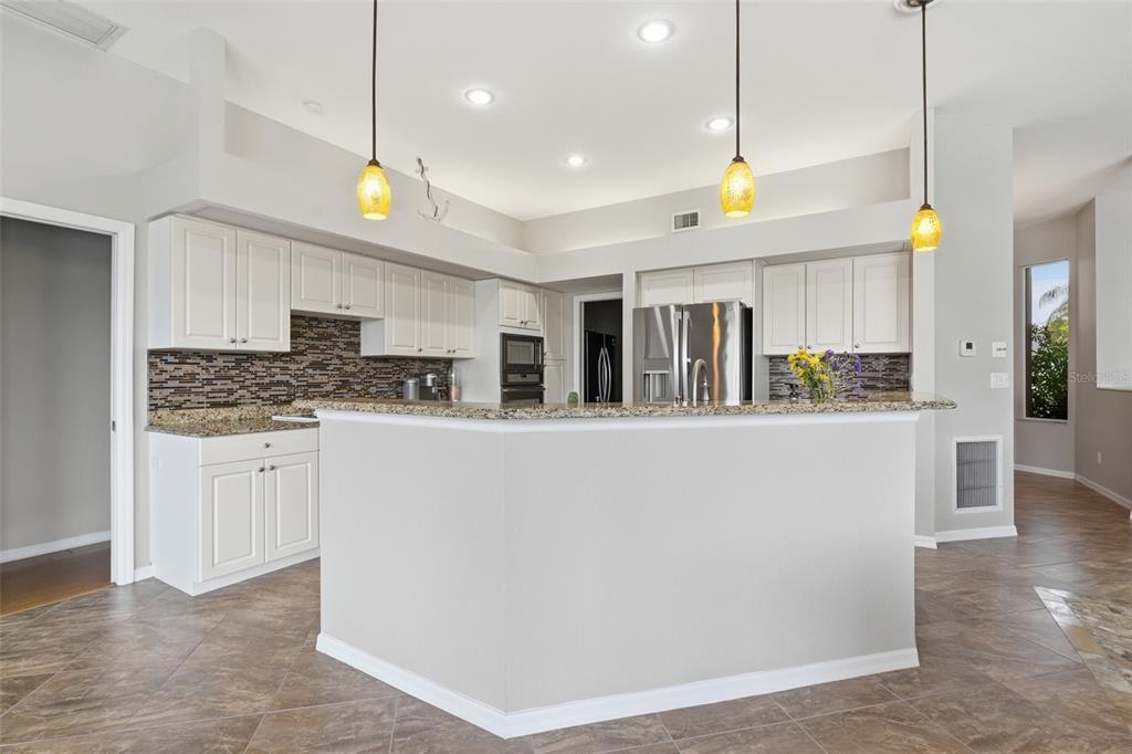 A kitchen with white cabinets, granite countertops, a tiled backsplash, and three hanging pendant lights — 5020 SW 8TH PLACE, CAPE CORAL, FL