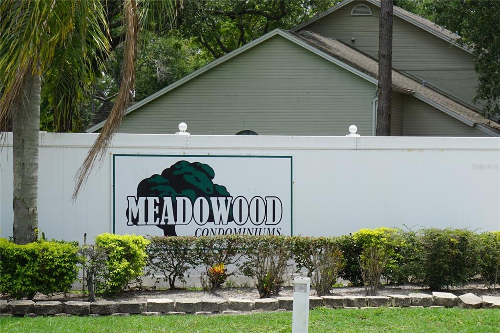 A white fence displays a sign for Meadowwood Condominiums in front of a residential building — 7807 AMBERLEA COURT UNIT 7807, TAMPA, FL