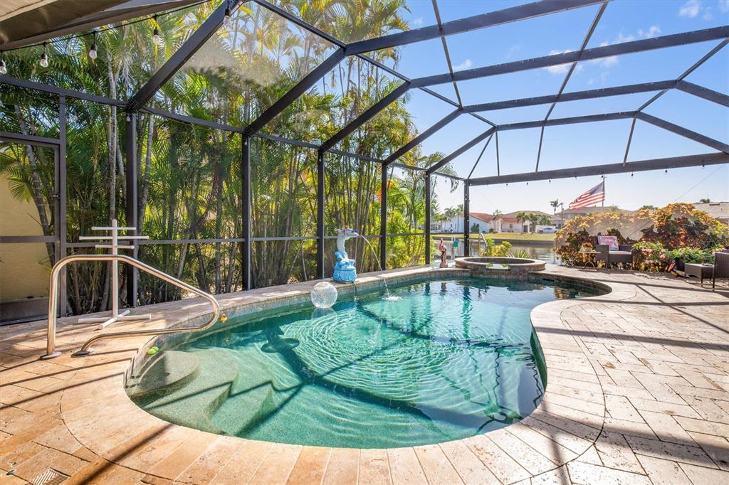 A screened-in pool area features a spa, stone decking, and a view of a canal — 590 TOULOUSE DRIVE, PUNTA GORDA, FL
