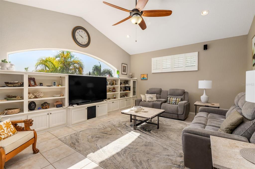 A living room features a large television, built-in shelving, gray sofas, and a ceiling fan — 590 TOULOUSE DRIVE, PUNTA GORDA, FL