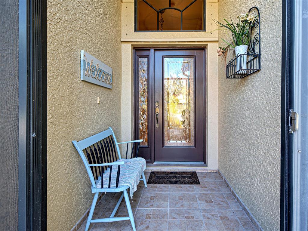 A light blue bench sits on a tiled porch in front of a glass-paneled door — 20612 CAPELLO DRIVE, VENICE, FL