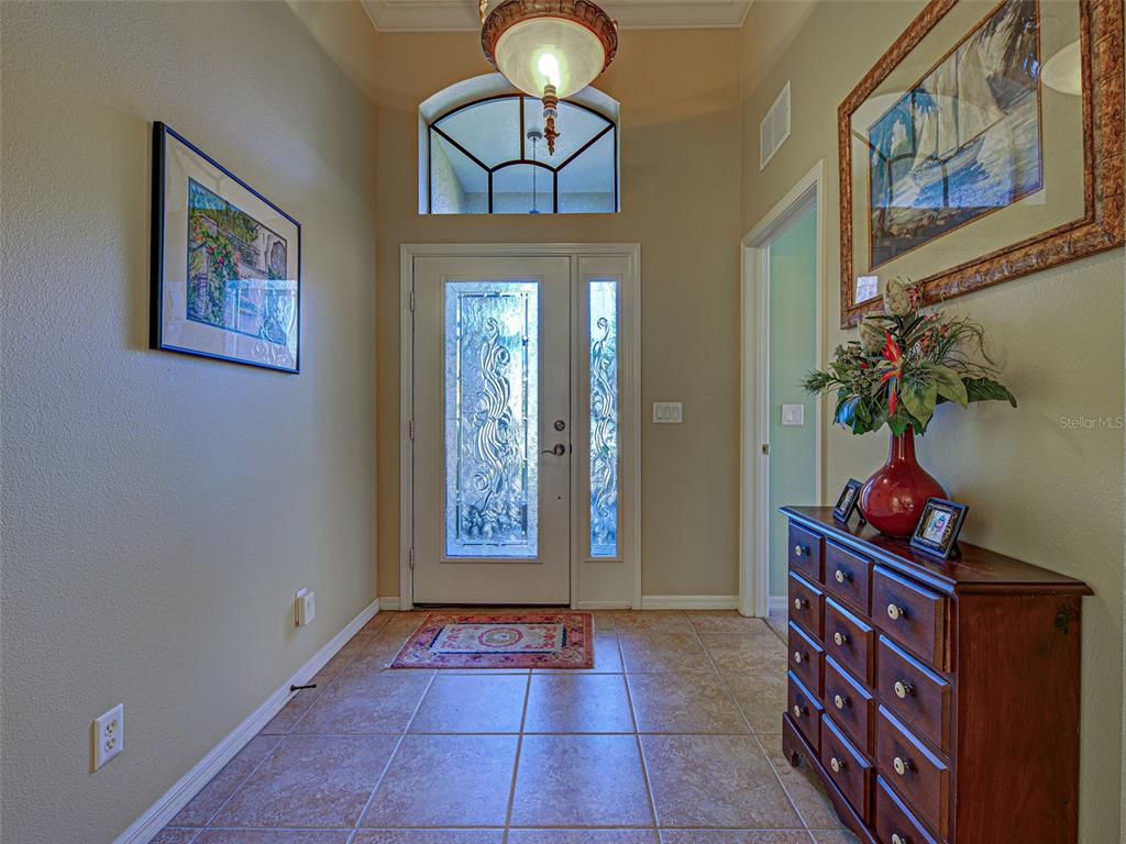 An entryway features tile flooring, a decorative front door with sidelights, and a wooden chest — 20612 CAPELLO DRIVE, VENICE, FL
