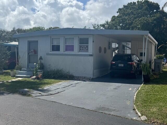 A single-story mobile home with a carport, driveway, and a for-sale sign in the window — 128 Havenwood Drive, Pompano Beach FL 33064, POMPANO BEACH, FL