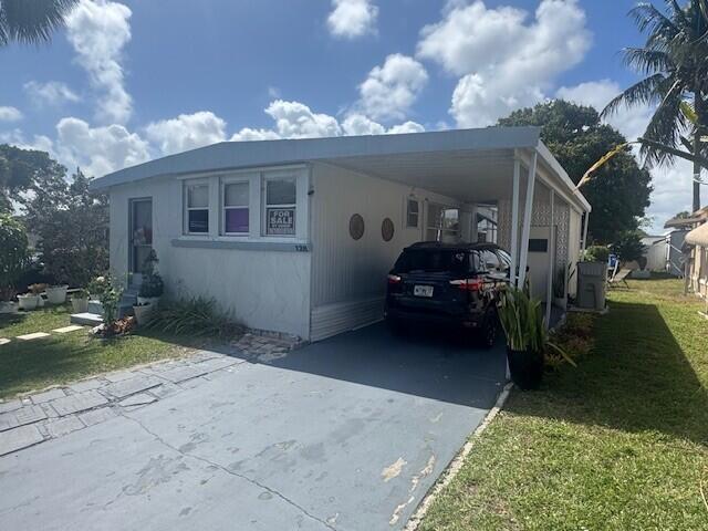 A single-story mobile home with a carport and a driveway under a blue sky — 128 Havenwood Drive, Pompano Beach FL 33064, POMPANO BEACH, FL