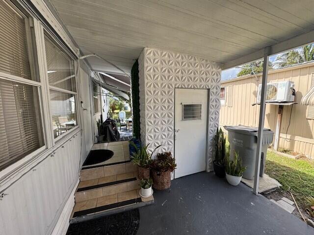 A covered patio features a textured white accent wall, a door, and tiled steps — 128 Havenwood Drive, Pompano Beach FL 33064, POMPANO BEACH, FL