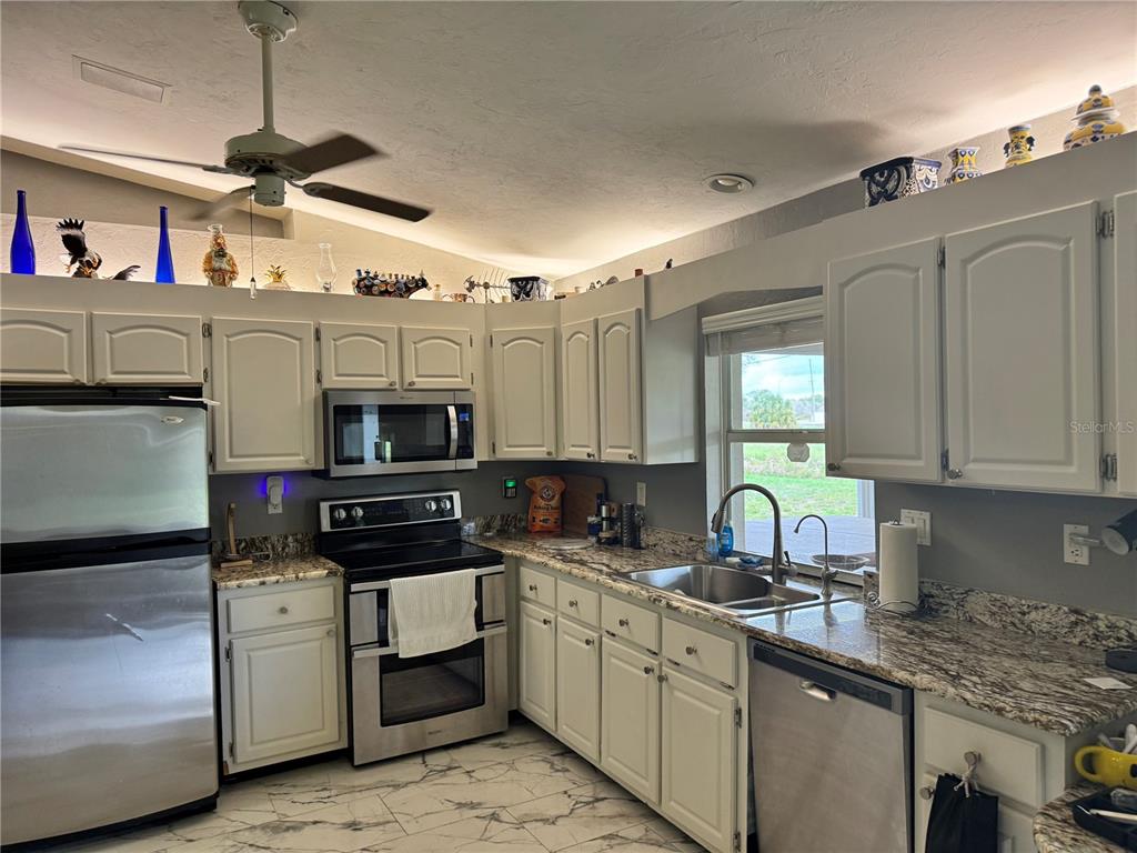A kitchen features white cabinets, granite countertops, stainless steel appliances, and a tiled floor — 30048 OAK ROAD, PUNTA GORDA, FL