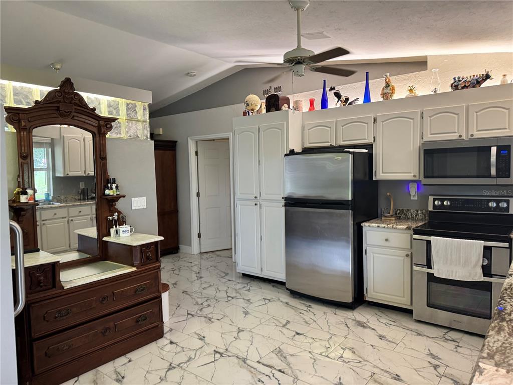 A kitchen features white cabinets, stainless steel appliances, and white marble-patterned tile flooring — 30048 OAK ROAD, PUNTA GORDA, FL