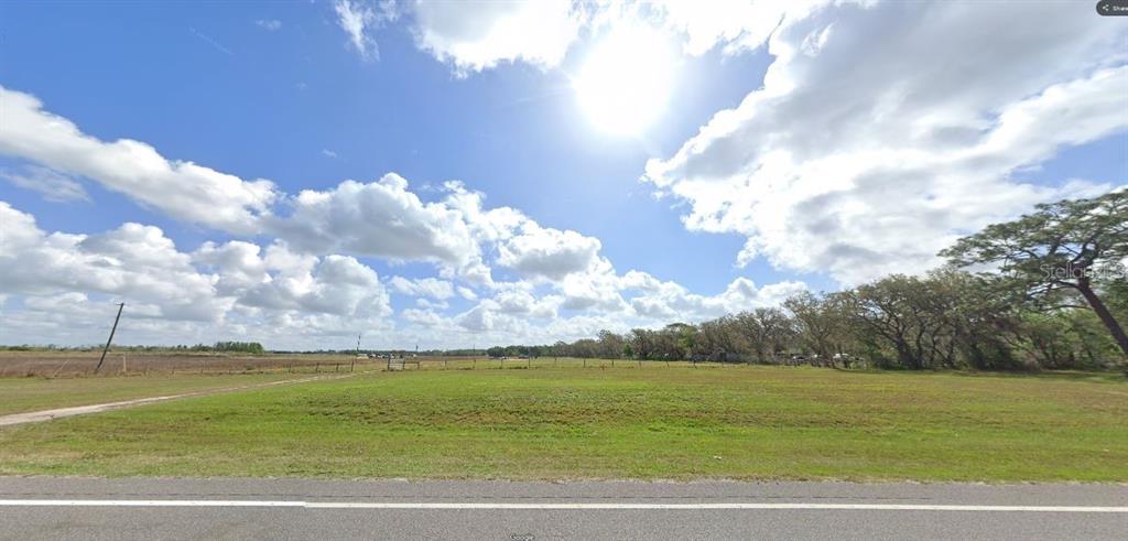 A wide, grassy vacant lot sits alongside a paved road under a bright, cloudy sky — COMMONWEALTH AVE N, POLK CITY, FL