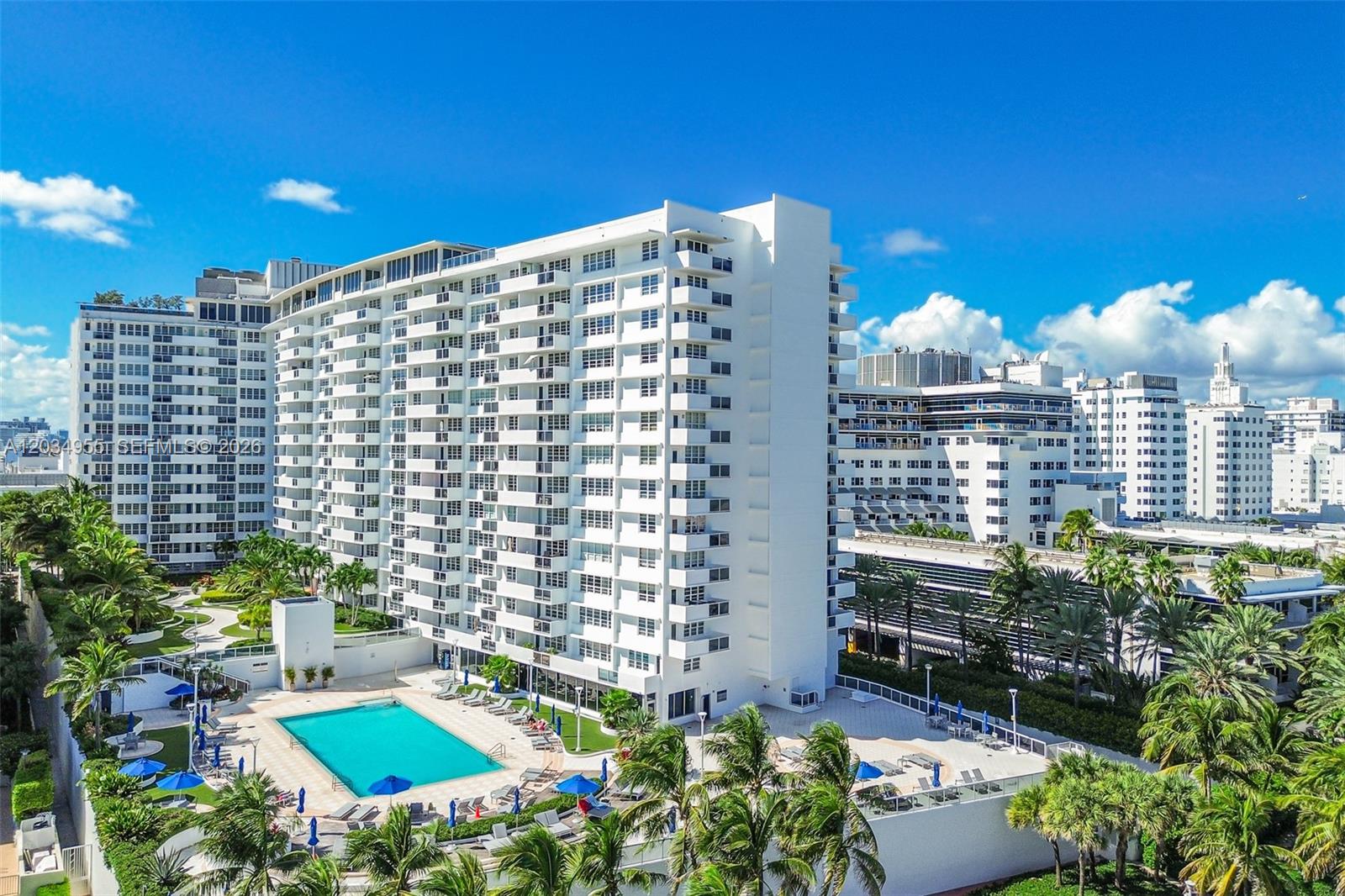An exterior view of a tall white apartment building with a swimming pool and palm trees — 100 Lincoln Rd # 502, Miami Beach FL 33139, MIAMI BEACH, FL