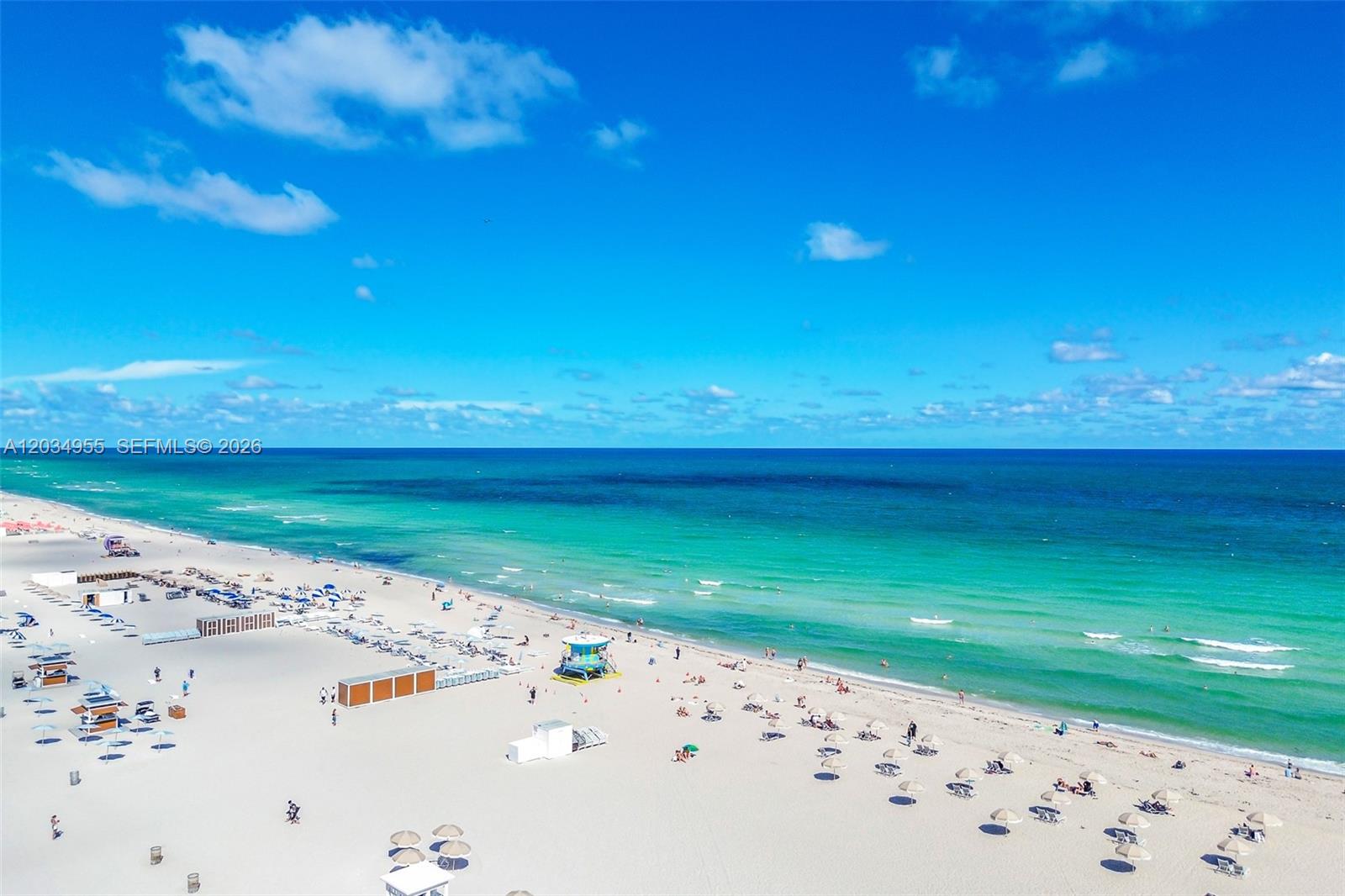 An aerial view shows a sandy beach with umbrellas, a lifeguard tower, and the ocean — 100 Lincoln Rd # 502, Miami Beach FL 33139, MIAMI BEACH, FL