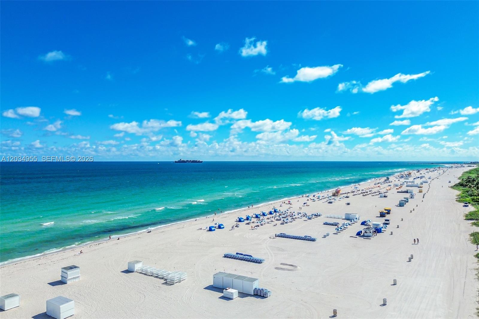 An aerial view shows a wide, sandy beach with blue umbrellas and white structures — 100 Lincoln Rd # 502, Miami Beach FL 33139, MIAMI BEACH, FL