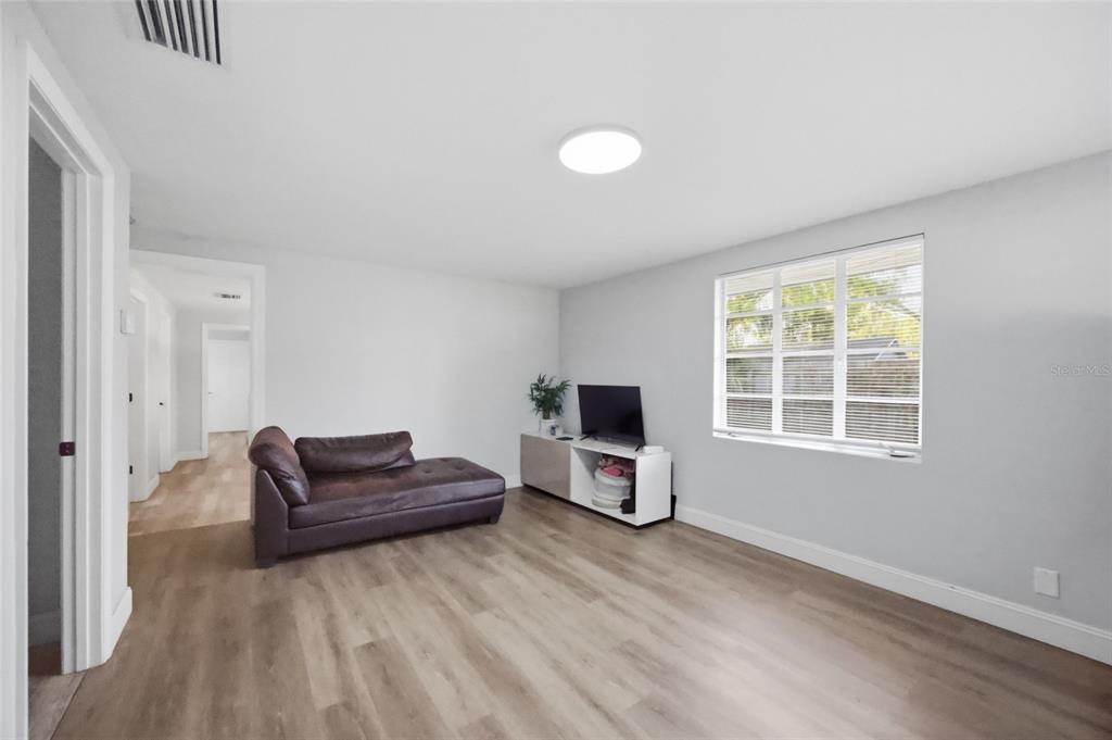 A living room features light wood-look flooring, a brown chaise sofa, and a television console — 907 CENTER STREET, PLANT CITY, FL
