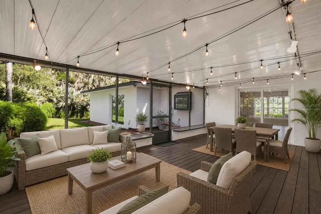 A covered outdoor patio features wicker furniture, a wooden dining set, and string lights — 10945 BIG TREE LANE, CLERMONT, FL