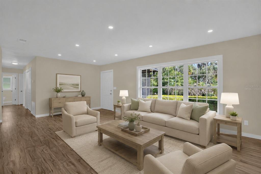 This virtually staged living room features light-colored furniture, a wooden coffee table, and large windows — 10945 BIG TREE LANE, CLERMONT, FL