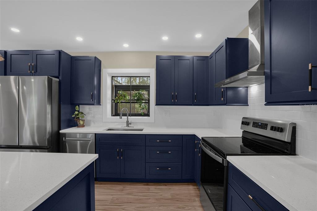 A kitchen features dark blue cabinets, white countertops, stainless steel appliances, and a window — 10945 BIG TREE LANE, CLERMONT, FL