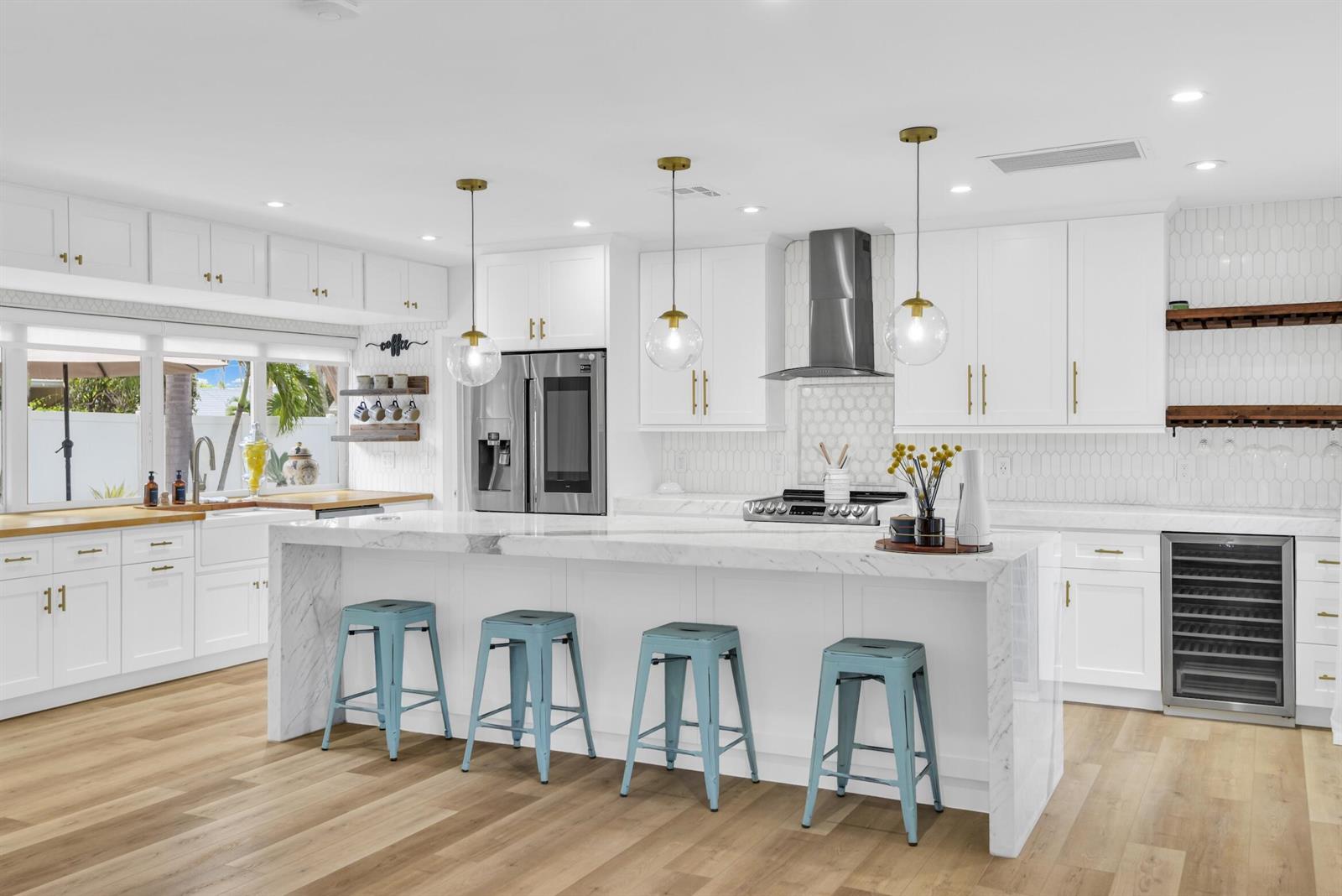A bright kitchen features a marble-topped island, white cabinetry, blue stools, and light wood flooring — 701 Appleby Street, Boca Raton FL 33487, BOCA RATON, FL