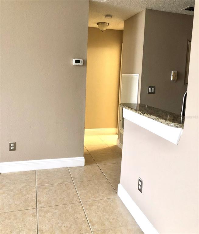 A tiled floor leads from a kitchen counter toward a hallway with a thermostat — 1055 S HIAWASSEE ROAD UNIT 2026, ORLANDO, FL