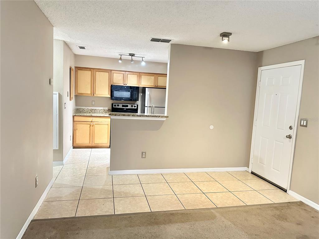A kitchen with light wood cabinets and tile flooring opens to a dining area — 1055 S HIAWASSEE ROAD UNIT 2026, ORLANDO, FL
