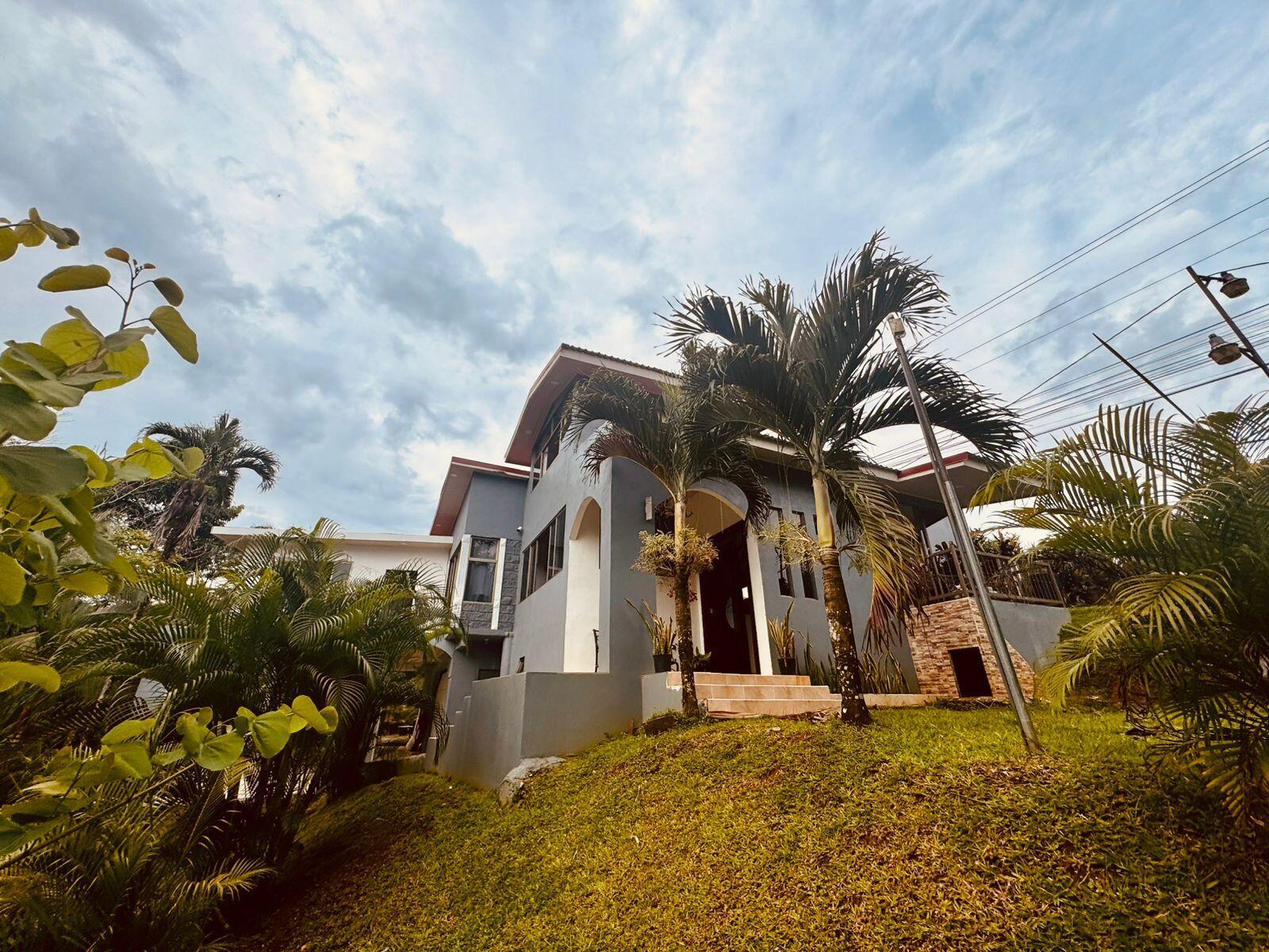 A two-story gray house with palm trees sits on a grassy hill under a cloudy sky — 141 N El Tanque Fortuna San Carlos Street, FL