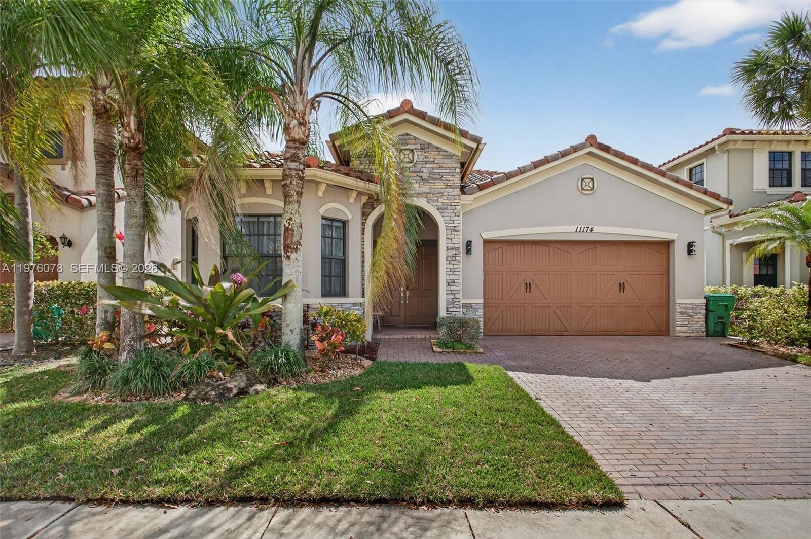 A single-story house with a stone-accented entryway, a brown garage door, and palm trees — 11174 NW 72nd Pl, Parkland FL 33076, PARKLAND, FL