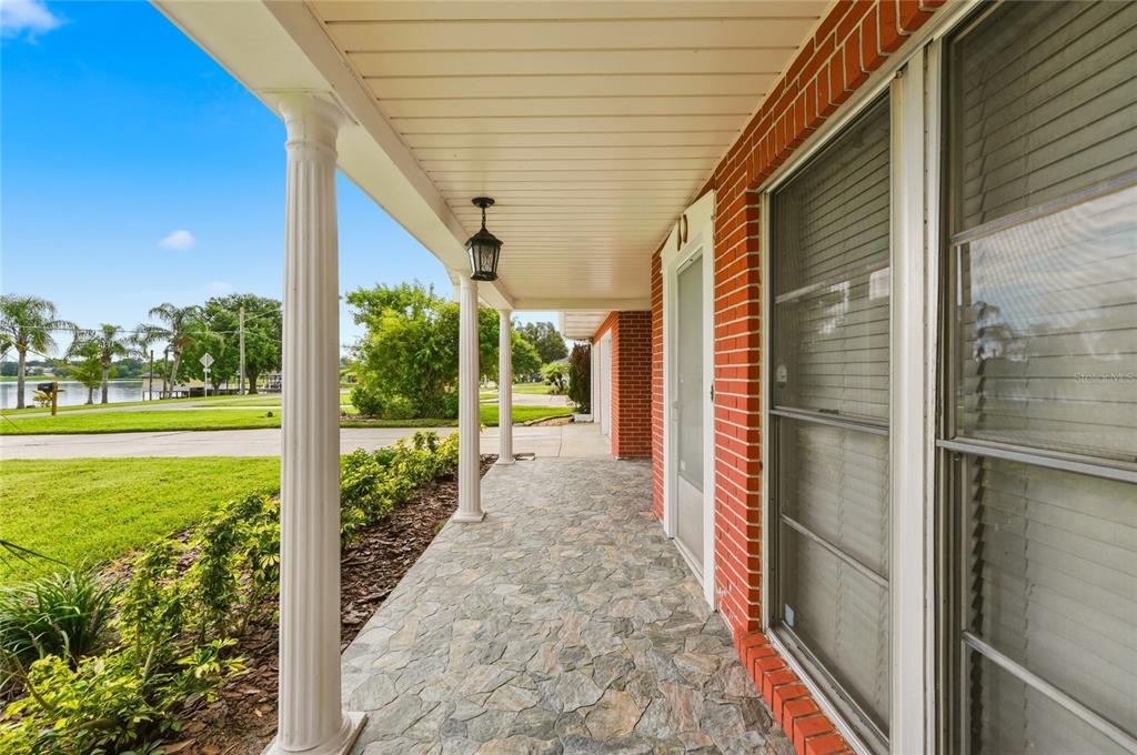A covered stone porch with white columns overlooks a grassy lawn and a distant lake — 1475 S LAKE HOWARD DRIVE, WINTER HAVEN, FL