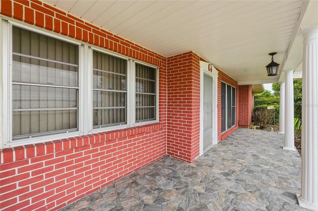A covered brick porch features stone flooring, white columns, and a front entrance door — 1475 S LAKE HOWARD DRIVE, WINTER HAVEN, FL