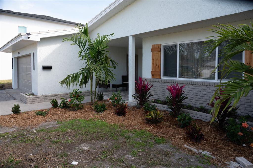 A white house exterior features a gray brick base, palm trees, and a front porch — 6613 BLUE HERON DRIVE S, ST PETERSBURG, FL