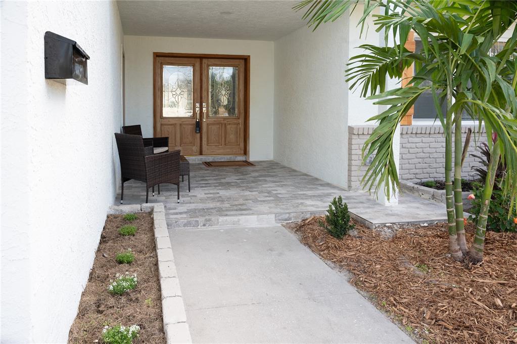 A paved entryway leads to a double wooden front door with glass inserts and seating — 6613 BLUE HERON DRIVE S, ST PETERSBURG, FL