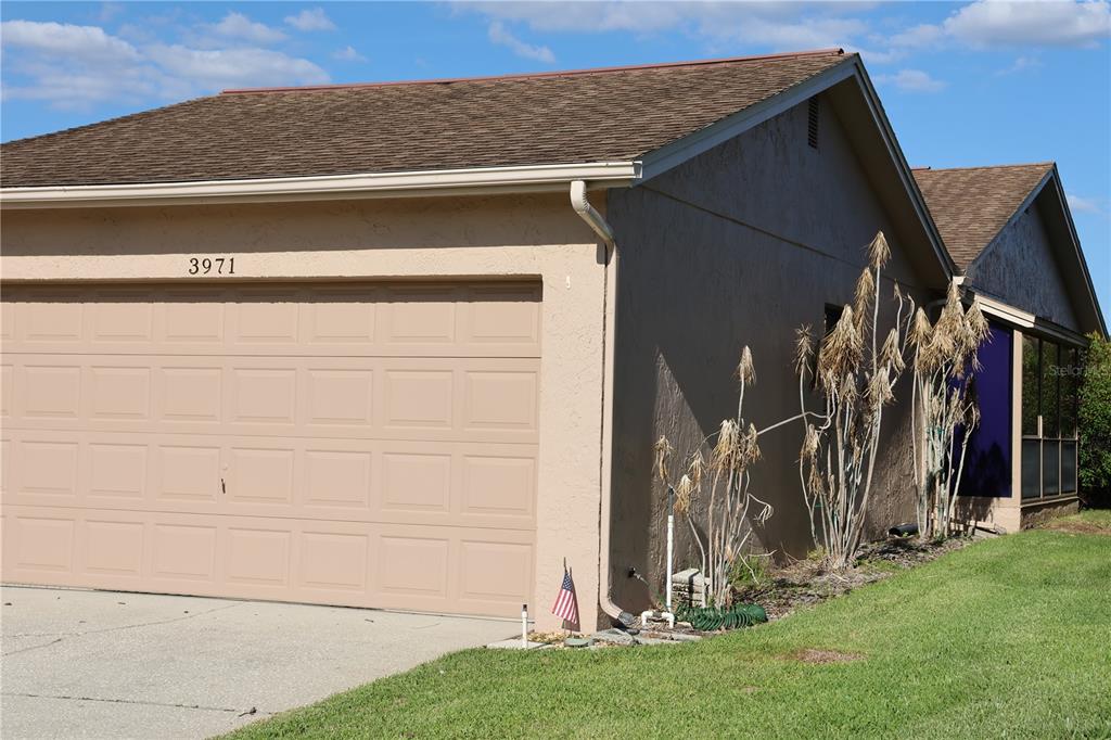 A beige house exterior features a two-car garage, a brown shingled roof, and dead landscaping — 3971 CYPRESS LANDING W, WINTER HAVEN, FL
