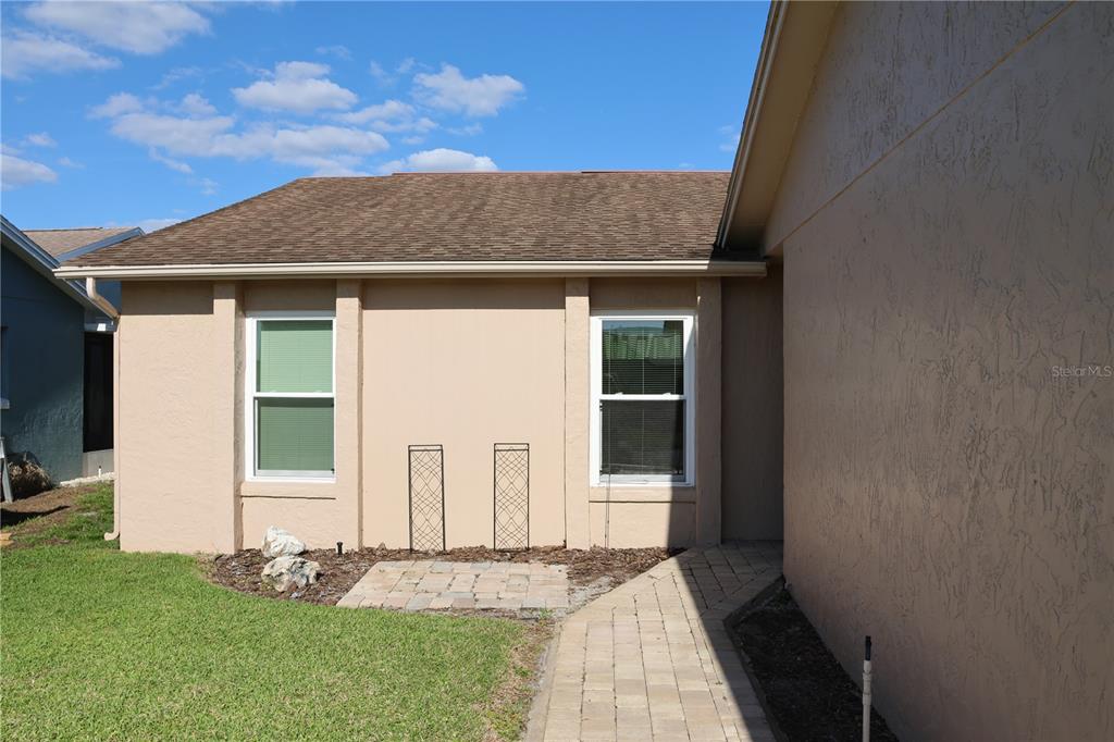 A tan stucco house exterior features two windows, a paver walkway, and two metal trellises — 3971 CYPRESS LANDING W, WINTER HAVEN, FL