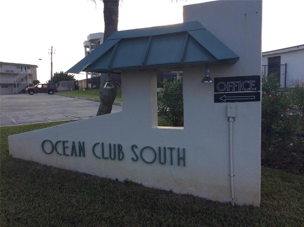 A concrete sign for Ocean Club South stands in a grassy area with an office sign — 4849 SAXON DRIVE UNIT C105, NEW SMYRNA BEACH, FL