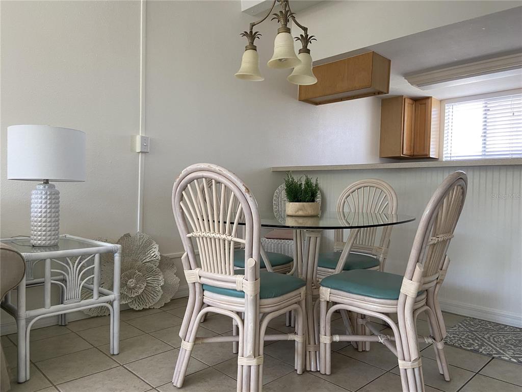 A dining area features a glass-topped table with four rattan chairs and a pendant light — 4849 SAXON DRIVE UNIT C105, NEW SMYRNA BEACH, FL