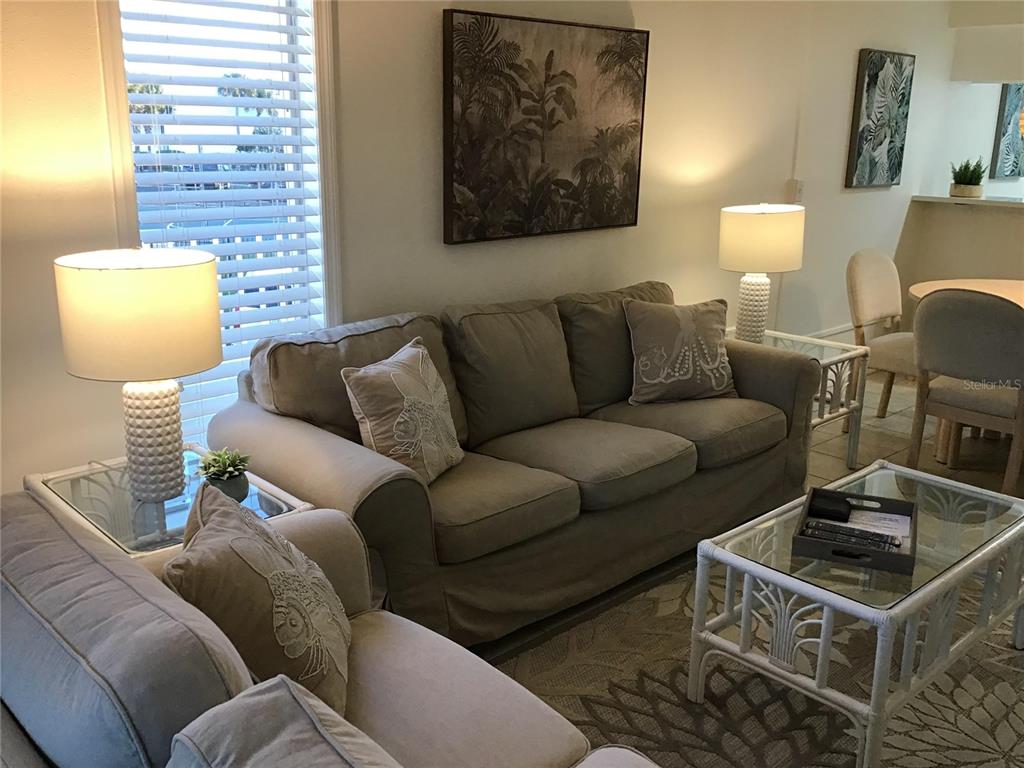 A living room features a beige sofa, glass-topped tables, and two lamps — 4849 SAXON DRIVE UNIT C105, NEW SMYRNA BEACH, FL