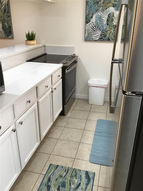 A kitchen features white cabinets, white countertops, stainless steel appliances, and tiled flooring — 4849 SAXON DRIVE UNIT C105, NEW SMYRNA BEACH, FL