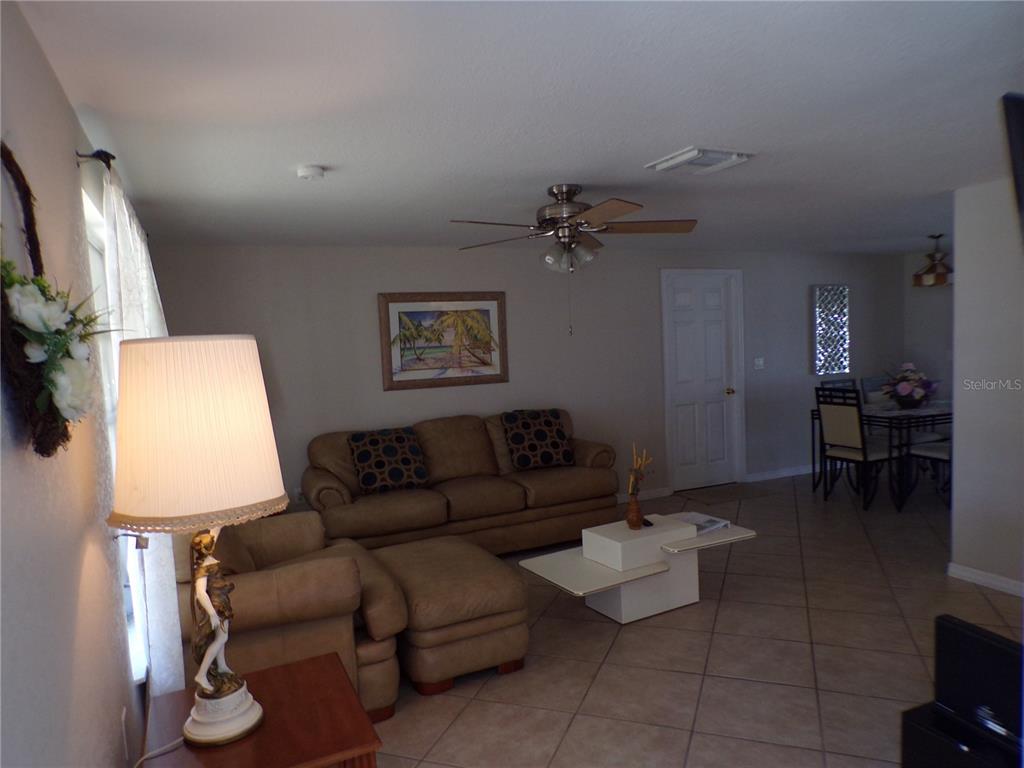 A living room with tan furniture, tile flooring, a ceiling fan, and an adjacent dining area — 182 CHELSEA COURT NW, PORT CHARLOTTE, FL