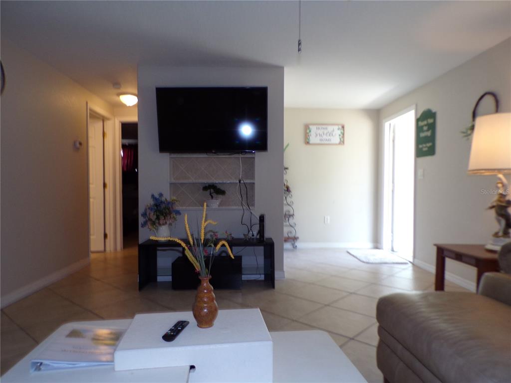 A living room features a wall-mounted television, a tiled floor, and a central entryway — 182 CHELSEA COURT NW, PORT CHARLOTTE, FL