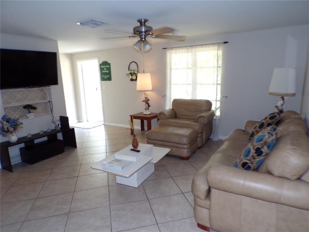 A living room features tile flooring, a ceiling fan, a television, and leather furniture — 182 CHELSEA COURT NW, PORT CHARLOTTE, FL