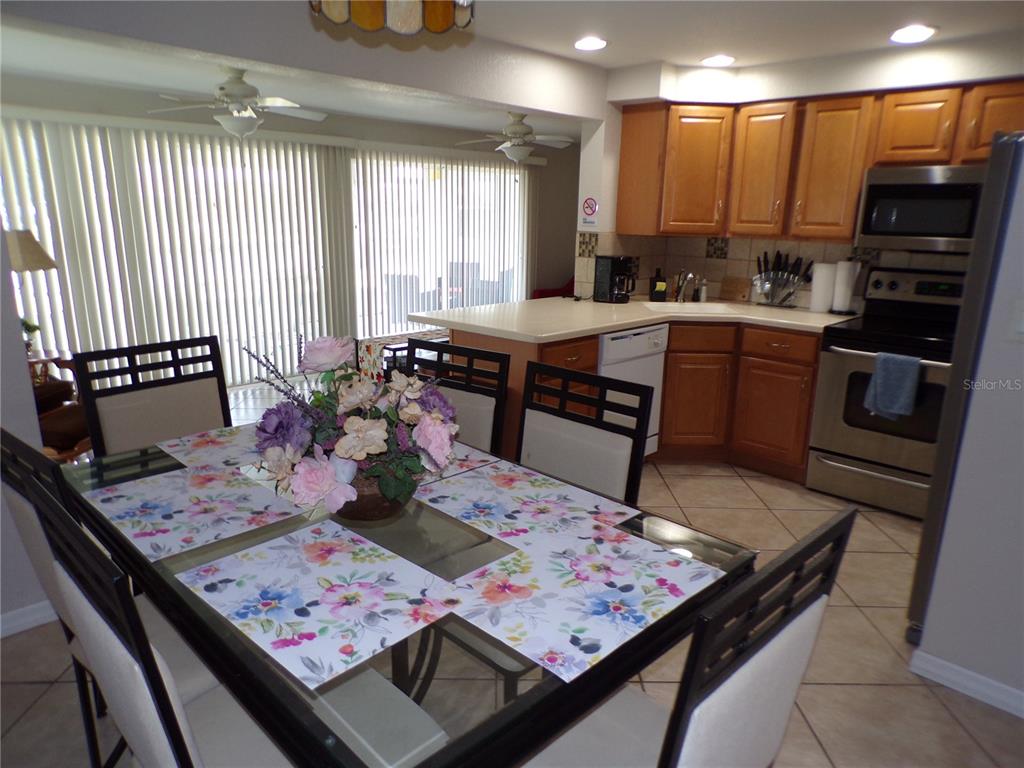 A dining area with a glass table sits adjacent to a kitchen with wooden cabinets — 182 CHELSEA COURT NW, PORT CHARLOTTE, FL