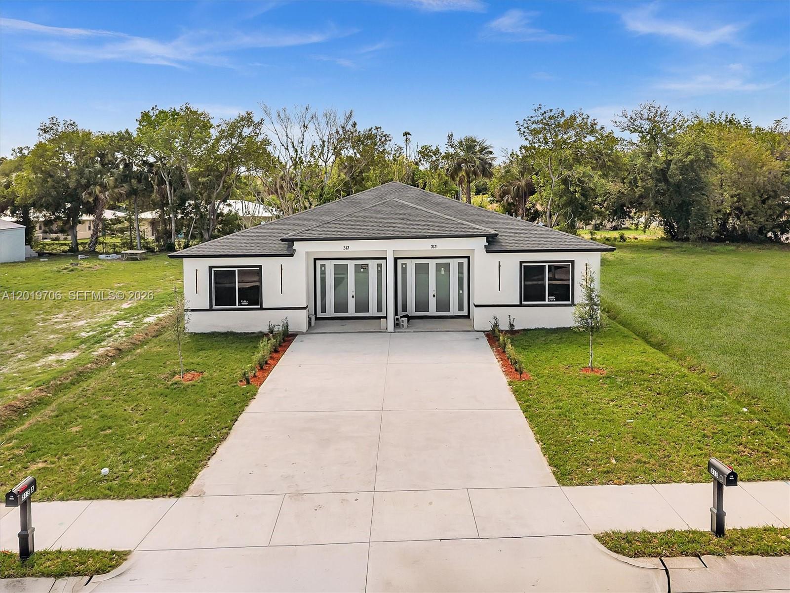 A modern, single-story duplex with a concrete driveway and two front entrances sits on grass — 313 S 13th St # A, Fort Pierce FL 34950, FORT PIERCE, FL