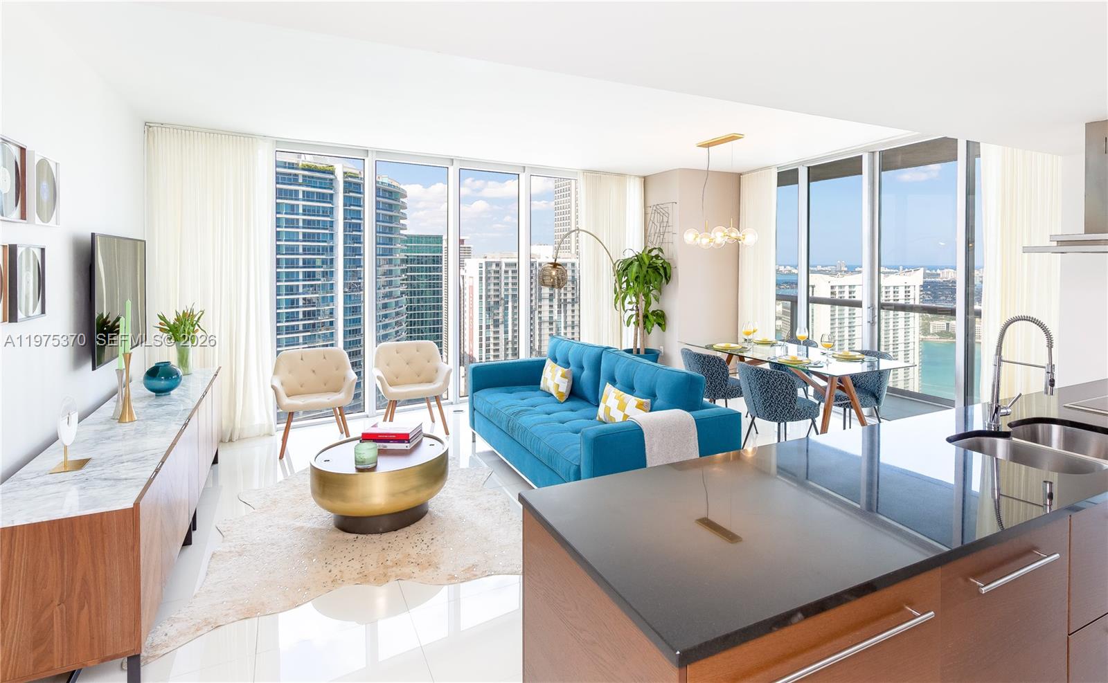 A modern open-plan living and dining area features a blue sofa, floor-to-ceiling windows, and city views — 485 Brickell Ave # 4702, Miami FL 33131, MIAMI, FL