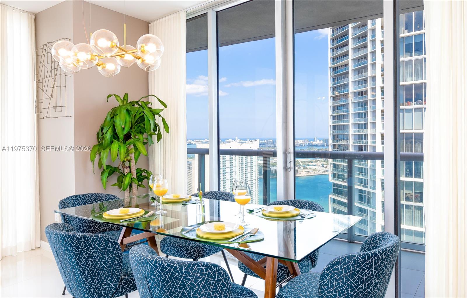 A dining area features a glass table, blue patterned chairs, and a view of skyscrapers — 485 Brickell Ave # 4702, Miami FL 33131, MIAMI, FL