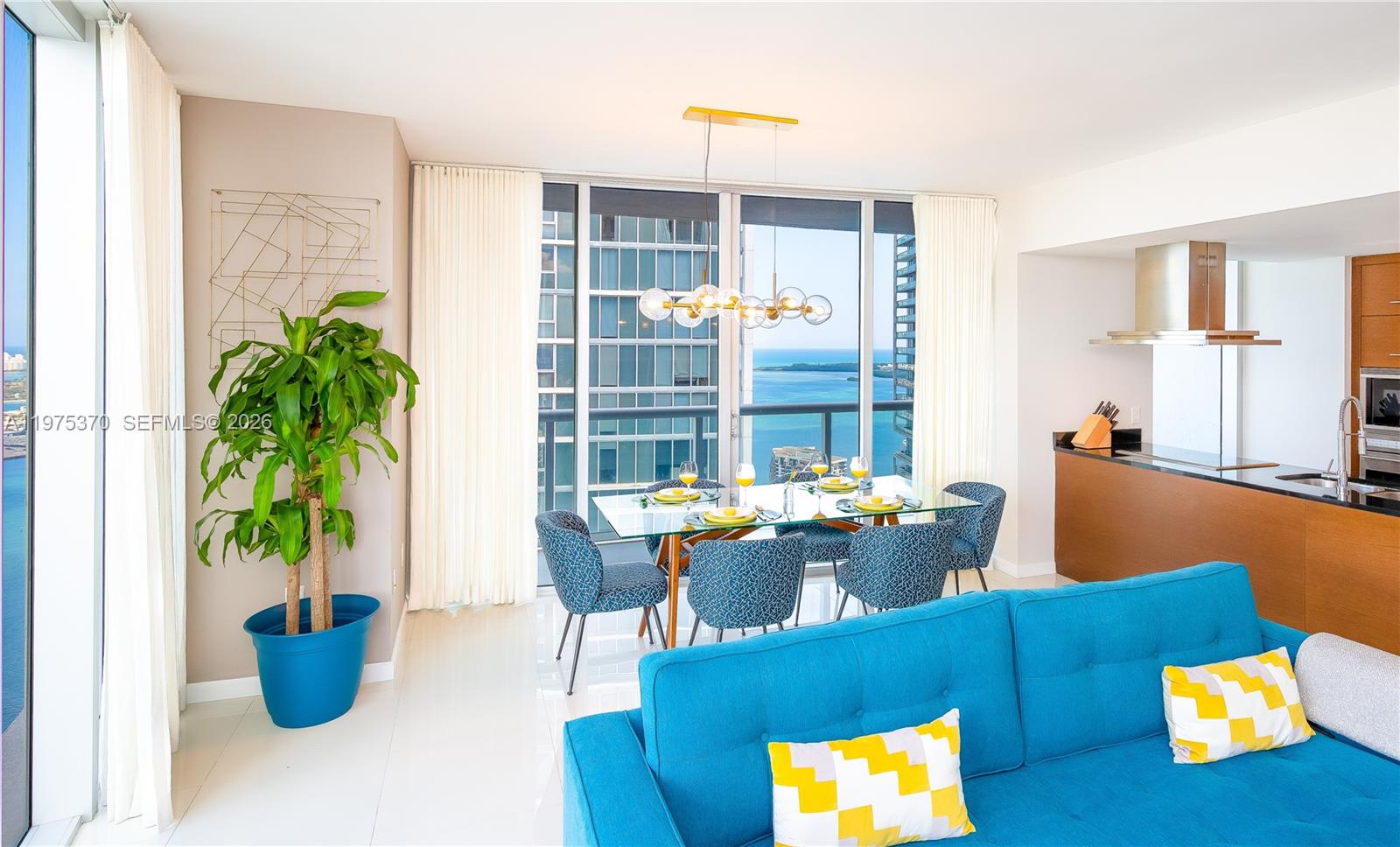 A modern dining area and living room feature a blue sofa, glass table, and ocean views — 485 Brickell Ave # 4702, Miami FL 33131, MIAMI, FL